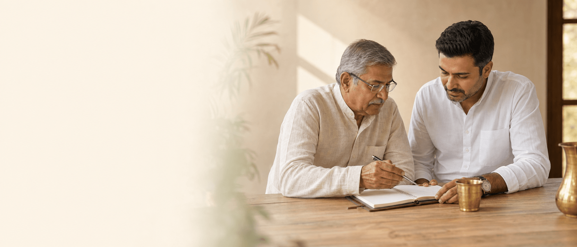 Two generations of Indian family-business leadership reviewing notes at a wooden table